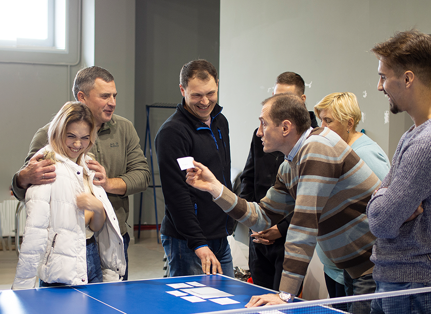 Group of people laughing and looking a blue table with cards